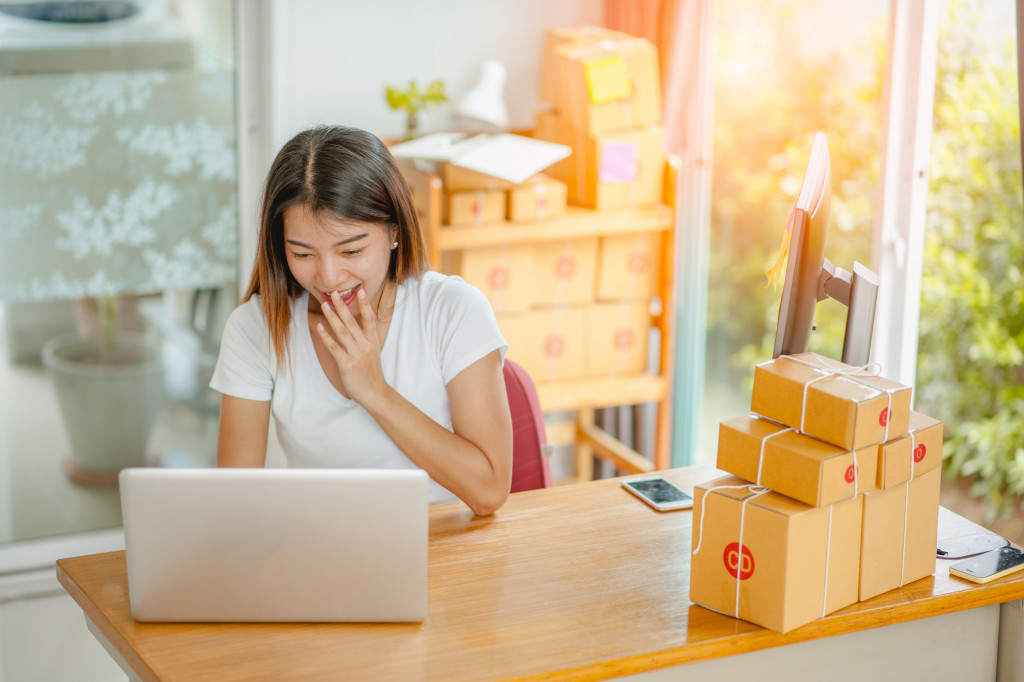 Young woman running an online business with her boxes on a table and behind her.