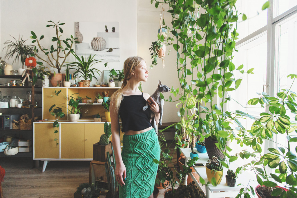 A woman holding a cat in a house full of green plants