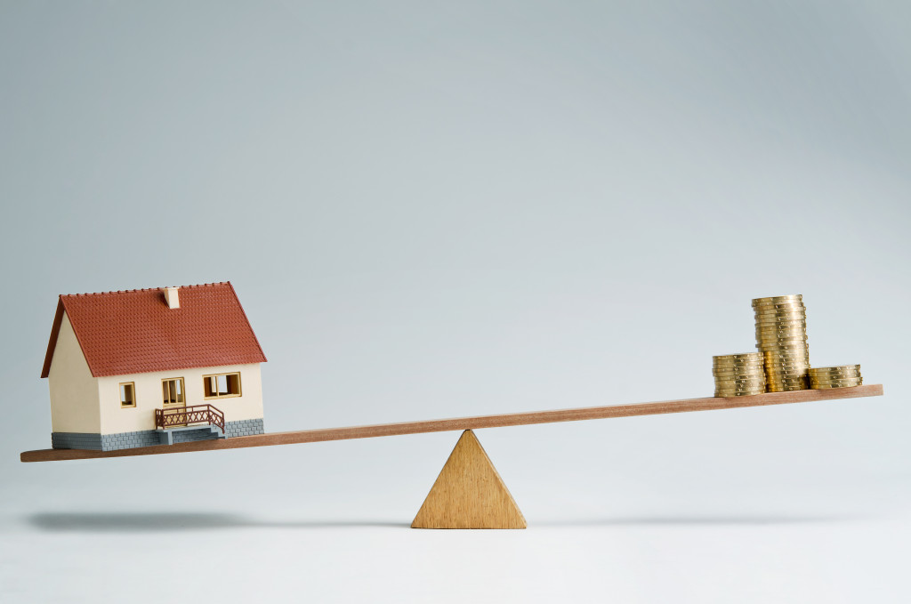 A model house and stacks of coins on opposite ends of a seesaw