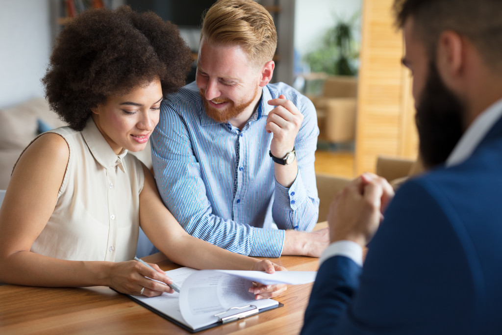 Young couple checking real estate documents on a table with an agent looking at them.