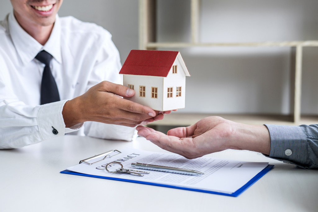 A real estate agent handing a model house to another persons hand after contract signing