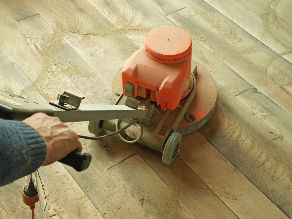 A person using an electric sander on a wooden floor