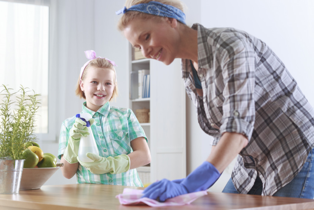 mother wiping the table with her daughter spraying the cleaning solution from the side