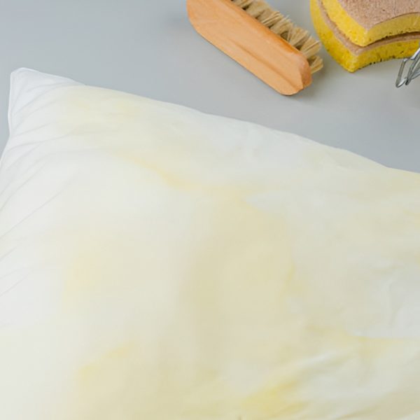pillow with yellow stains, jar of baking soda, sponge, and brush